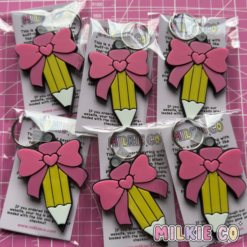 Pink bow and pencil keychains on white cards with visible brand name on a pink grid background